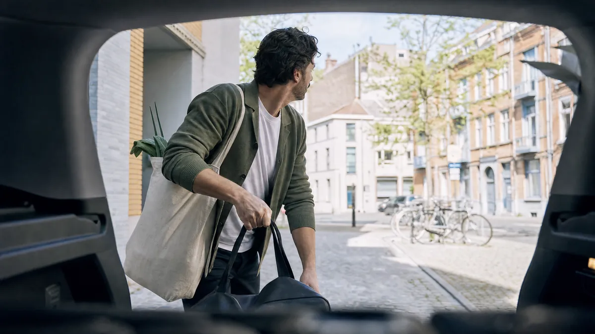 Man met reistassen bij de open koffer van een elektrische wagen in een Gentse straat