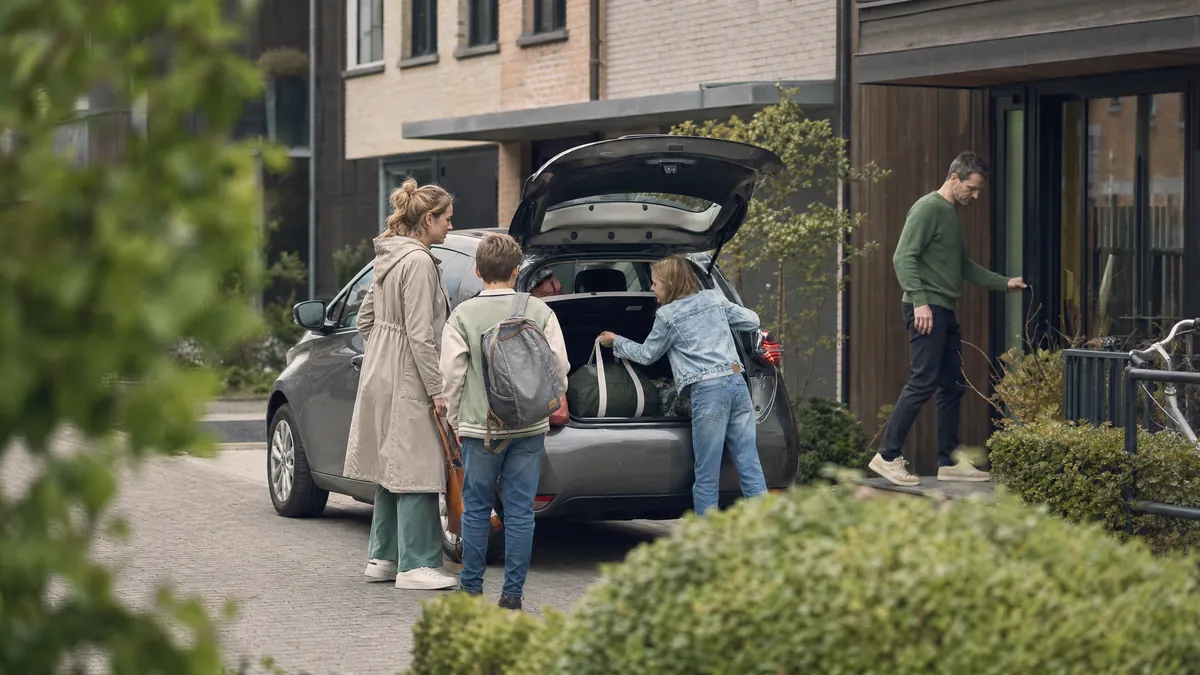 Een gezin laadt boodschappen in de koffer van een elektrische wagen voor hun woning