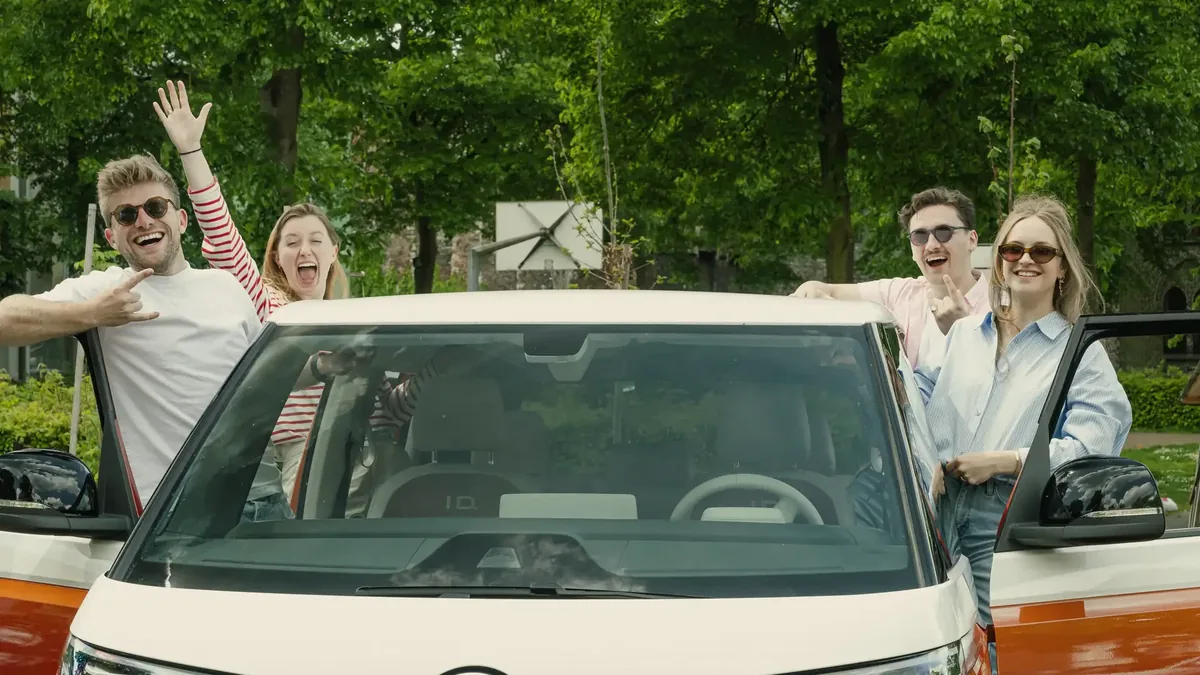 Vier vrienden zwaaien bij een oranje-witte Volkswagen ID.Buzz in een park